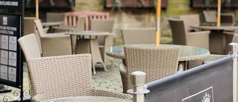 Outdoor wicker tables and chairs, a banner with 'The Rutland Arms' logo, and umbrellas.