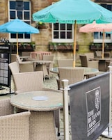 Mesas y sillas de mimbre al aire libre, un cartel con el logotipo de 'The Rutland Arms' y sombrillas.