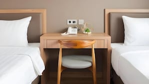 Habitación de hotel con dos camas, un escritorio de madera, una silla y una mesita de noche con una lámpara y una pequeña planta.