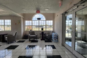 A lobby with a checkered floor, two armchairs, a small table, and a large window with a view of the outside.