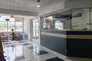 A reception area with a check-in counter, a seating area with chairs, and a large window providing a view outside. - Classic Inn San Marcos, TX (Calumet Park)