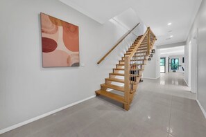 Un interior modern amb una escala de fusta, un gran quadre abstracte i un passadís lluminós.