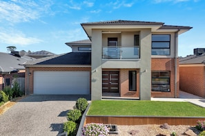 Een woonhuis met twee verdiepingen, een garage, een balkon en een keurig onderhouden gazon.