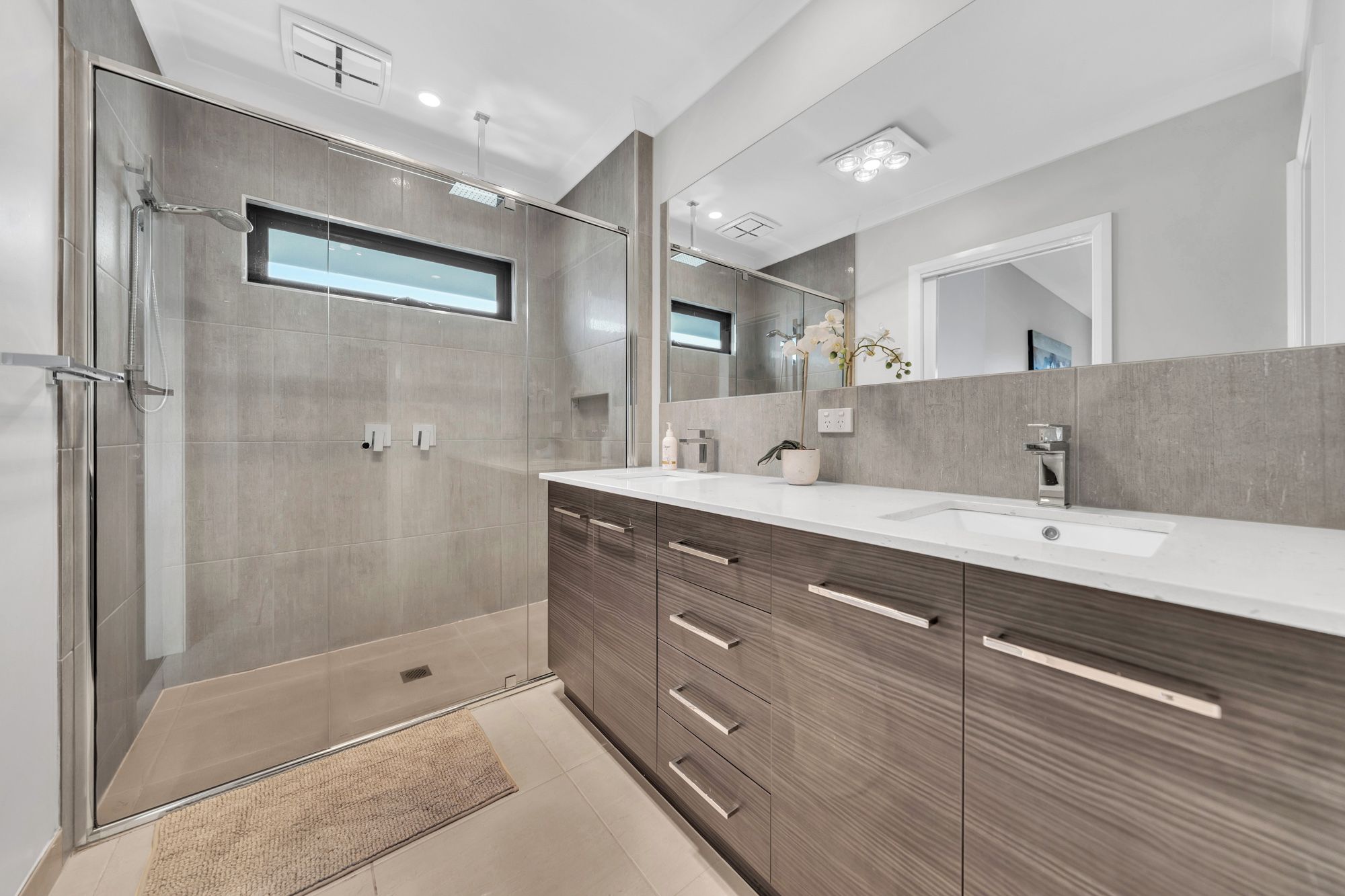 Un baño moderno con ducha a nivel, un espejo grande y un mueble de tocador con lavamanos.