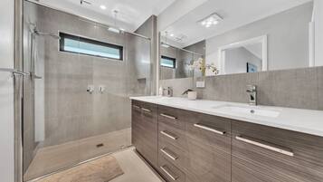 Un baño moderno con ducha a nivel, un espejo grande y un mueble de tocador con lavamanos.