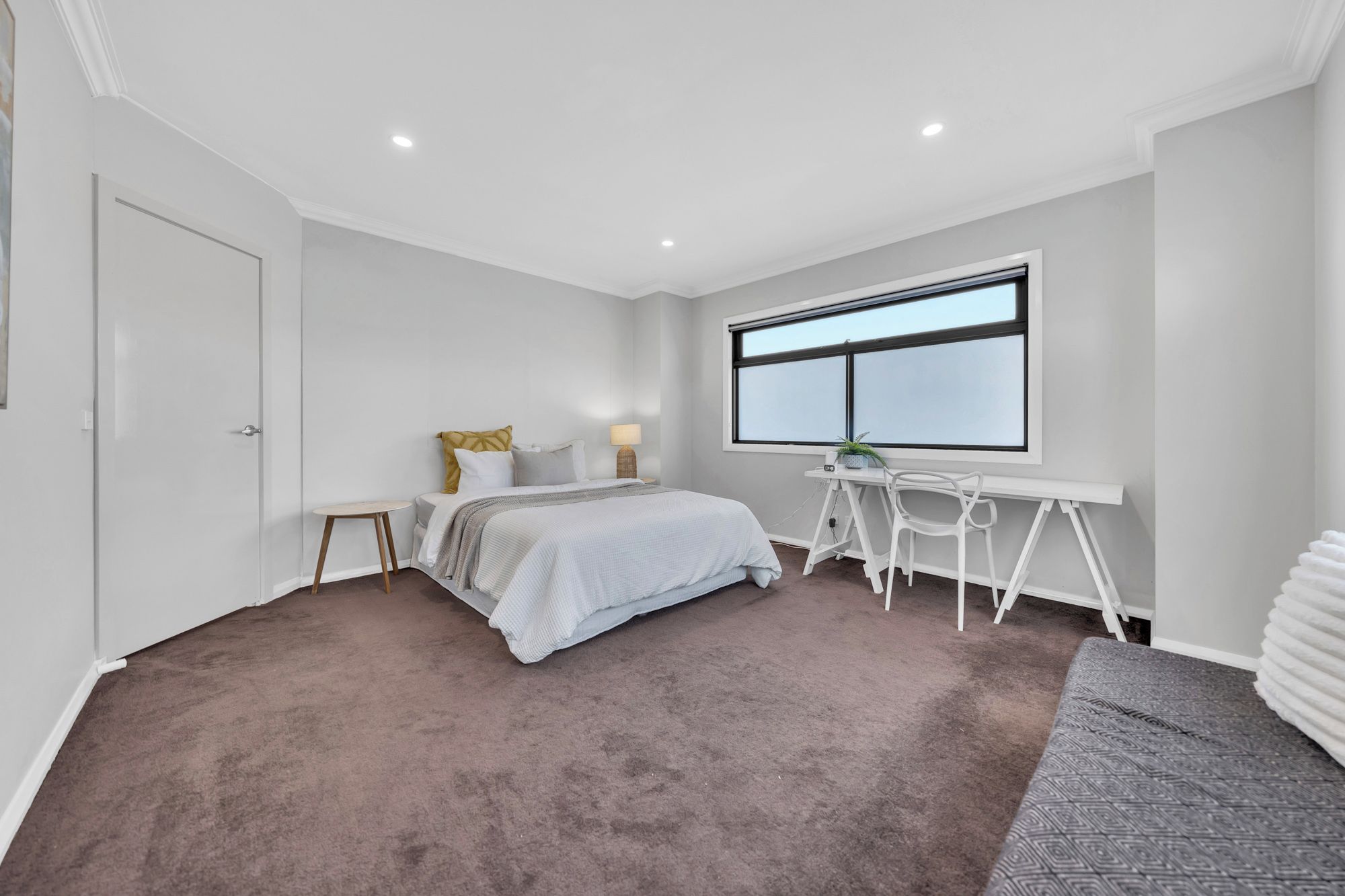 A bedroom with a bed, a desk, a chair, a window, and a door.