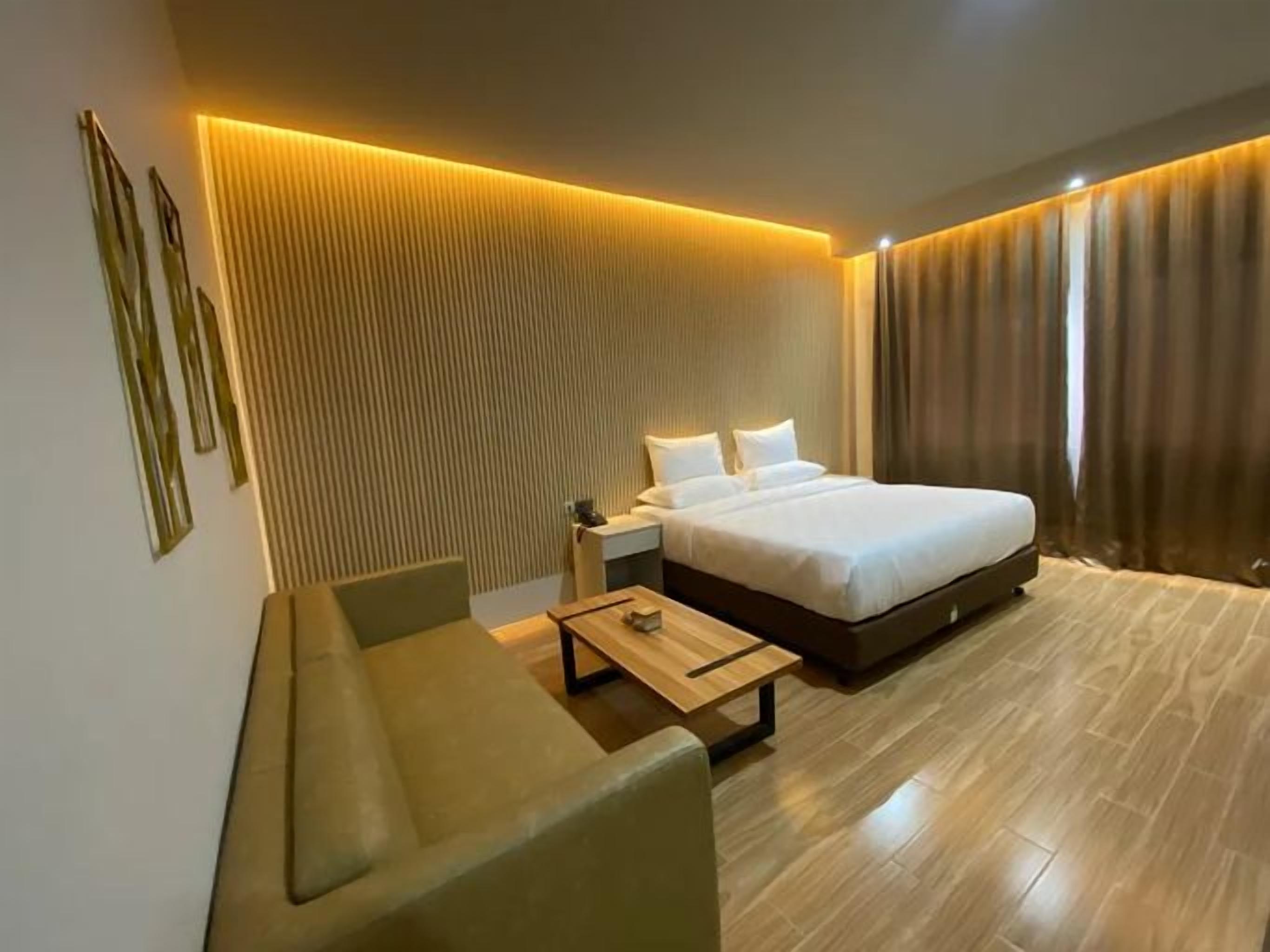 A modern hotel room with a large bed, a seating area with a table, and a wall-mounted light fixture.