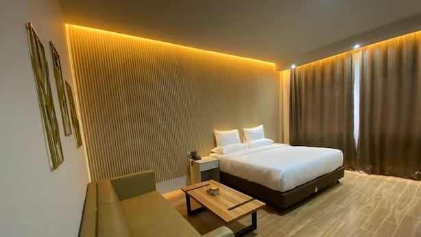 Ein modernes Hotelzimmer mit einem großen Bett, einer Sitzecke mit Tisch und einer wandmontierten Lampe.