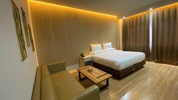 A modern hotel room with a large bed, a seating area with a table, and a wall-mounted light fixture.
