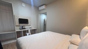 Ein Hotelzimmer mit einem Bett, einem Schreibtisch mit Flachbildfernseher, einem Kleiderschrank und einer Klimaanlage.