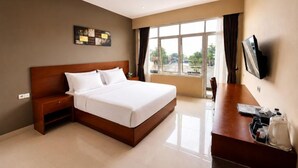 A hotel room with a large bed, a desk, a flat-screen TV, and a window with curtains. - Grand Kanaya Baturraden (Baturaden)