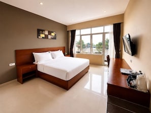 Habitación de hotel con una cama grande, un escritorio, un televisor de pantalla plana y un ventanal con cortinas.