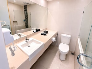 Un baño moderno con un espejo grande, un lavamanos, un inodoro y una zona de ducha.