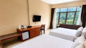 A hotel room with two beds, a desk, a television, and a window with curtains. - Grand Kanaya Baturraden (Baturaden)