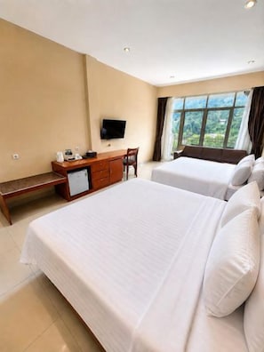 Habitación de hotel con dos camas, un escritorio, un televisor y una ventana con cortinas.