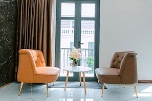 A room with two armchairs, a small round table with a vase of flowers, and a view of a building through a door. - VIN Hotel (Phuoc Hau)