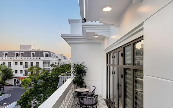 A balcony with a table and chairs, overlooking a street with buildings and trees. - VIN Hotel (Phuoc Hau)