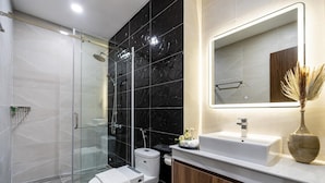 A modern bathroom with a glass-enclosed shower, a white toilet, a vanity with a mirror, and a vase with dried plants. - VIN Hotel (Phuoc Hau)