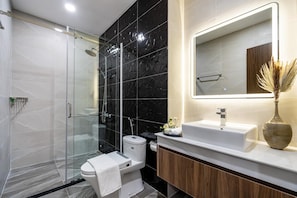 Et moderne badeværelse med et glasvægshus, et hvidt toilet, en vask med et spejl og en vase med tørrede planter.