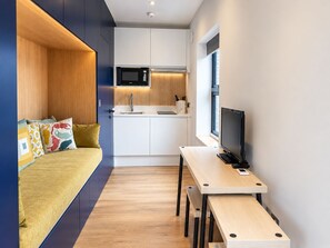 A compact living space with a kitchenette, a bed with colorful pillows, a desk with a computer, and a window. - Cosy Studio Flat in Gipsy Hill - Pass the Keys (London)