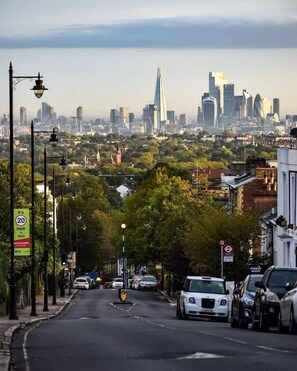 A city street with parked cars, a speed limit sign, and a view of the skyline. - Cosy Studio Flat in Gipsy Hill - Pass the Keys (London)