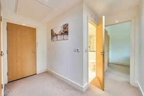 Ein Flur mit einer Holztür, einem Gemälde und einer offenen Tür zu einem Badezimmer.