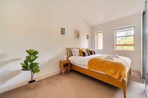 Ein Schlafzimmer mit einem Bett, einem Nachttisch, einer Lampe, einer Topfpflanze und einem Fenster.