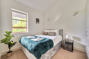 A bedroom with a bed, a bedside table, a nightstand, a potted plant, and a window with blinds. - Surrey's Stylish 2-Bed | Parking | Near Station - Pass the Keys (Surrey)
