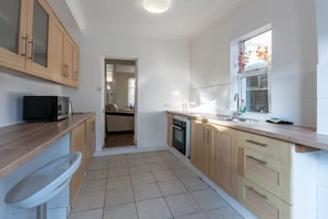 A compact kitchen with wooden cabinets, a microwave, a sink, and a window with a view. - 3BR home in Southend | Sleeps 8 - Pass the Keys (Southend-on-Sea)