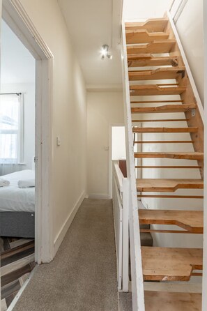 A staircase with wooden steps and a carpeted floor leading to a bedroom with a bed and a window. - 3BR home in Southend | Sleeps 8 - Pass the Keys (Southend-on-Sea)