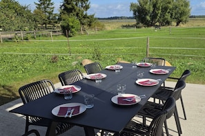 An outdoor dining area with a table set for six, surrounded by chairs, in a grassy field with trees and a fence in the background. - For 8 guests: entire floor with a garden on the Peenestrom (Kröslin)