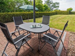 Eine Terrasse mit einem runden Tisch und vier Stühlen, einer Tablett mit Tassen und einem Teekännchen, sowie einem grünen Sonnenschirm.