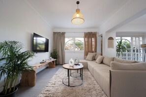 Ein modernes Wohnzimmer mit einer Couch, einem Couchtisch, einem Fernseher und einem großen Fenster mit Vorhängen.