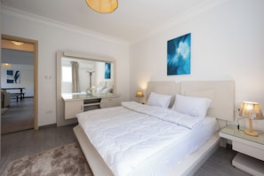 Ein modernes Schlafzimmer mit einem großen Bett, einem Nachttisch mit Lampe, einem Spiegel über der Kommode und Bildern an der Wand.