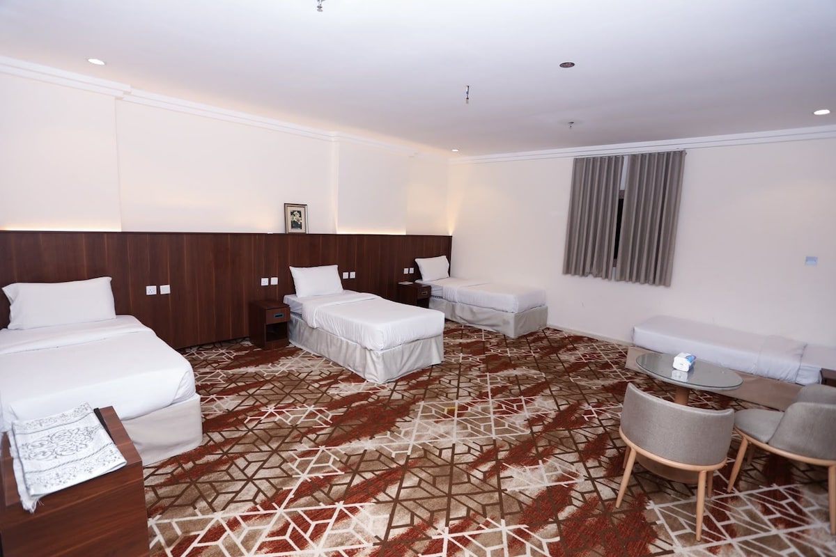 A hotel room with two beds, a sofa, a small table, and a patterned carpet.