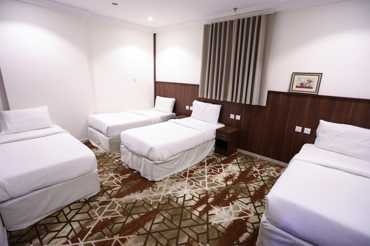 A hotel room with three beds, a wooden headboard, a patterned carpet, and a window with curtains.
