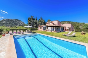 A swimming pool with lounge chairs, a house, and a mountainous backdrop. - Vrbo Property (Pollenca)
