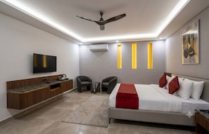 Une chambre d’hôtel moderne équipée d’un lit, d’un coin salon, d’un téléviseur à écran plat, d’un ventilateur de plafond et d’un climatiseur mural.