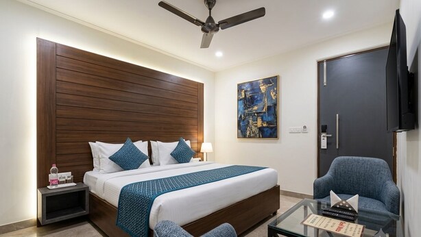 Ein Hotelzimmer mit einem Bett, einem Sessel, einem Glastisch, einem Deckenventilator, einem Gemälde und einem Fernseher.