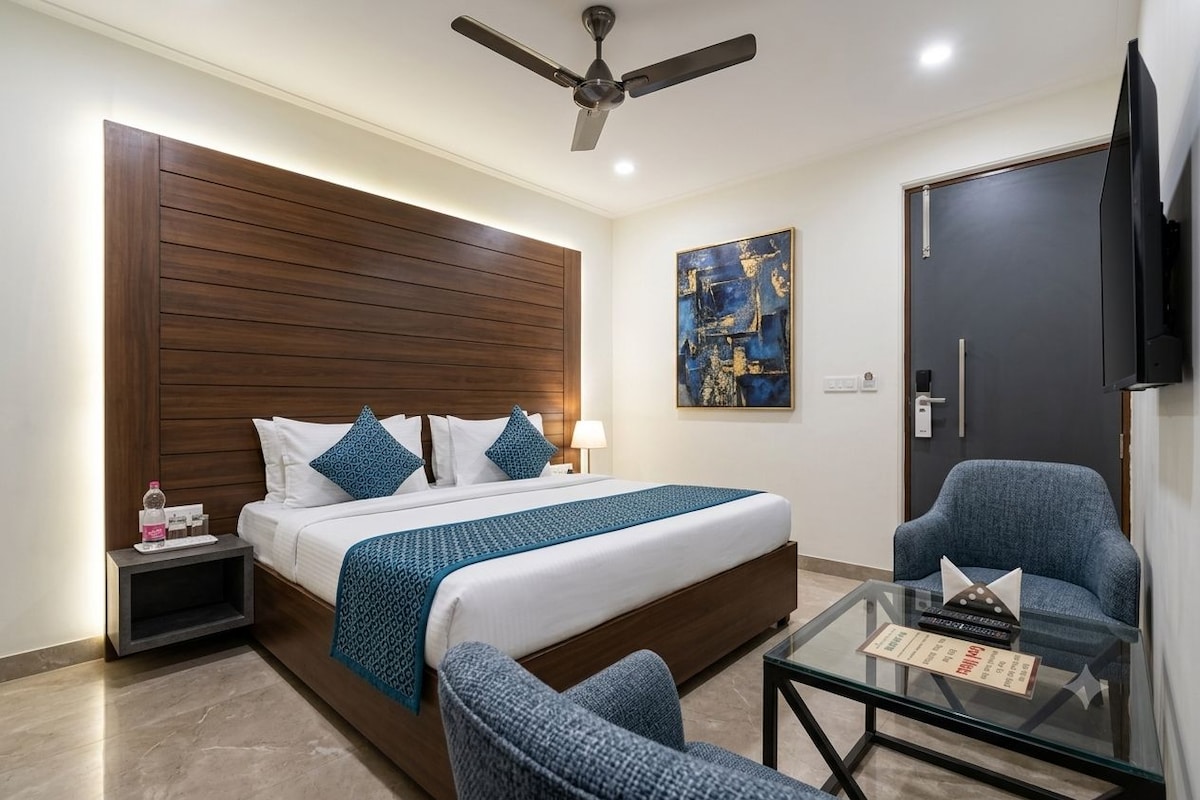 Une chambre d’hôtel avec un lit, une chaise, une table en verre, un ventilateur de plafond, un tableau et un téléviseur.
