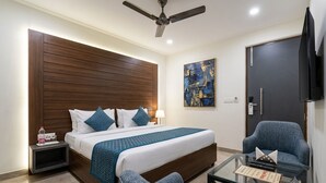 Ein Hotelzimmer mit einem Bett, einem Sessel, einem Glastisch, einem Deckenventilator, einem Gemälde und einem Fernseher.