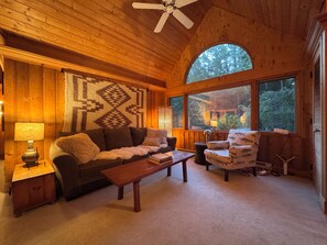 A cozy room with a wooden ceiling, a large window, a sofa, a chair, a lamp, and a patterned rug. - Treehouse like escape in North Asheville (Woodfin)