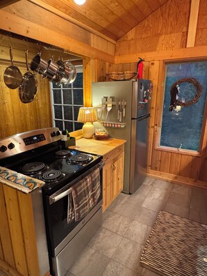 A kitchen with wooden walls, a stove, a refrigerator, and hanging pots. - Treehouse like escape in North Asheville (Woodfin)