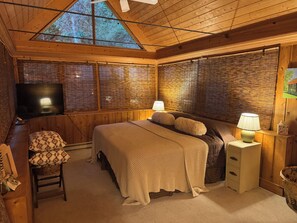 A cozy bedroom with a large bed, a television, and a window with blinds. - Treehouse like escape in North Asheville (Woodfin)