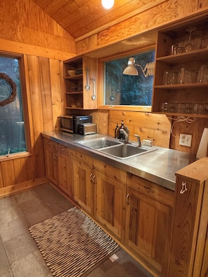 A wooden cabin kitchen with a double sink, a microwave, and a window overlooking a forest. - Treehouse like escape in North Asheville (Woodfin)