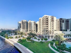 A high-rise residential building with multiple balconies, a swimming pool, and a well-maintained lawn. - Soothing 1BR Retreat with Access to a Man-Made Lagoon (Dubai)
