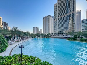 Ein Pool mit Liegestühlen und Palmen, umgeben von Hochhäusern.