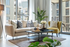 A modern living room with a sofa, armchair, coffee table, and a potted plant. - Soothing 1BR Retreat with Access to a Man-Made Lagoon (Dubai)