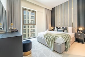 A modern bedroom with a large window, a bed with a green throw, and a bedside table with a lamp. - Soothing 1BR Retreat with Access to a Man-Made Lagoon (Dubai)