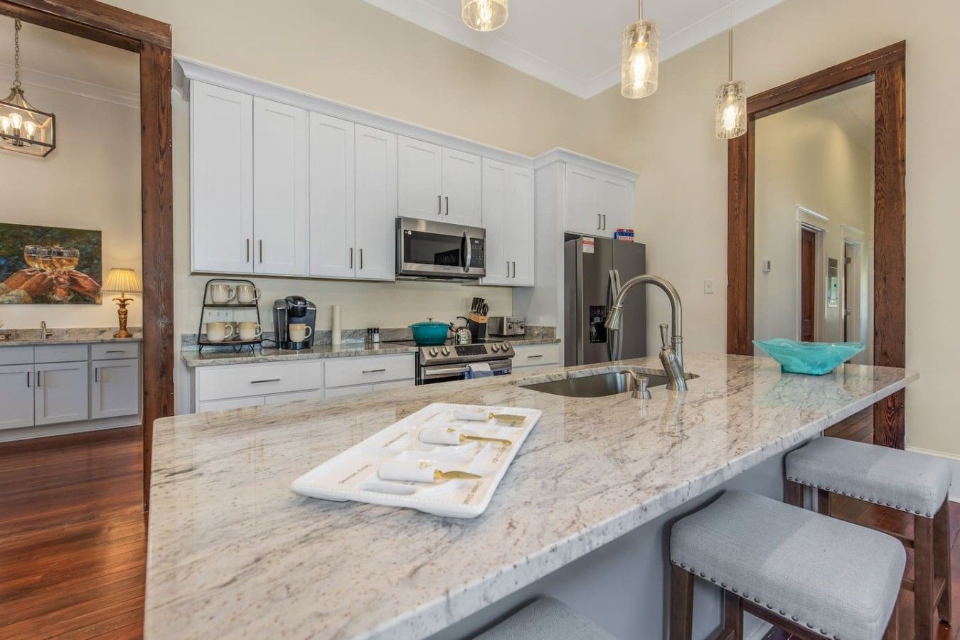 A modern kitchen with white cabinets, a central island with bar stools, stainless steel appliances, and pendant lighting.
